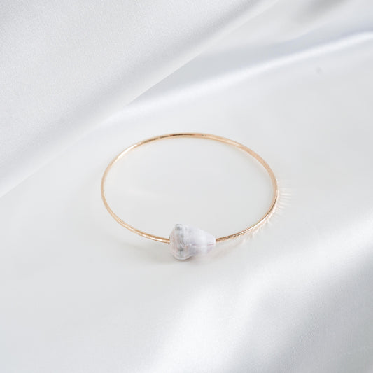 Gold bracelet with a white cone shell on a white background