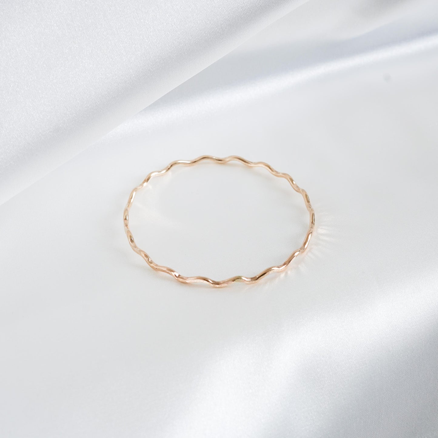 Gold wavy bracelet on a white satin background