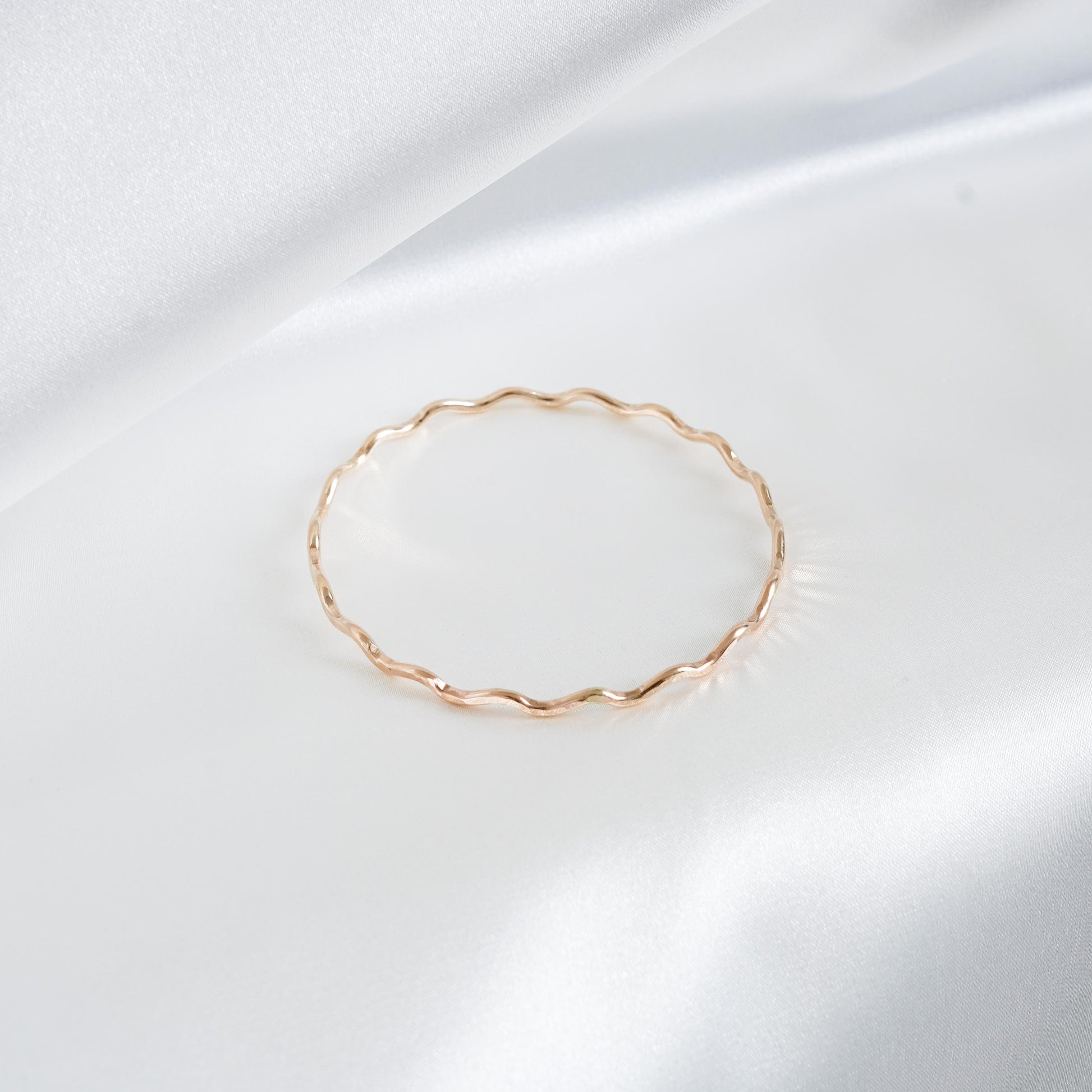 Gold wavy bracelet on a white satin background