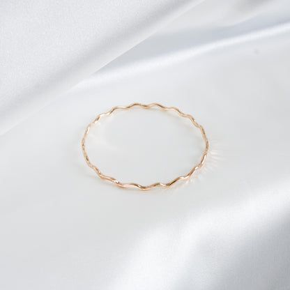 Gold wavy bracelet on a white satin background