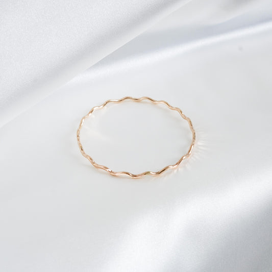 Gold wavy bracelet on a white satin background