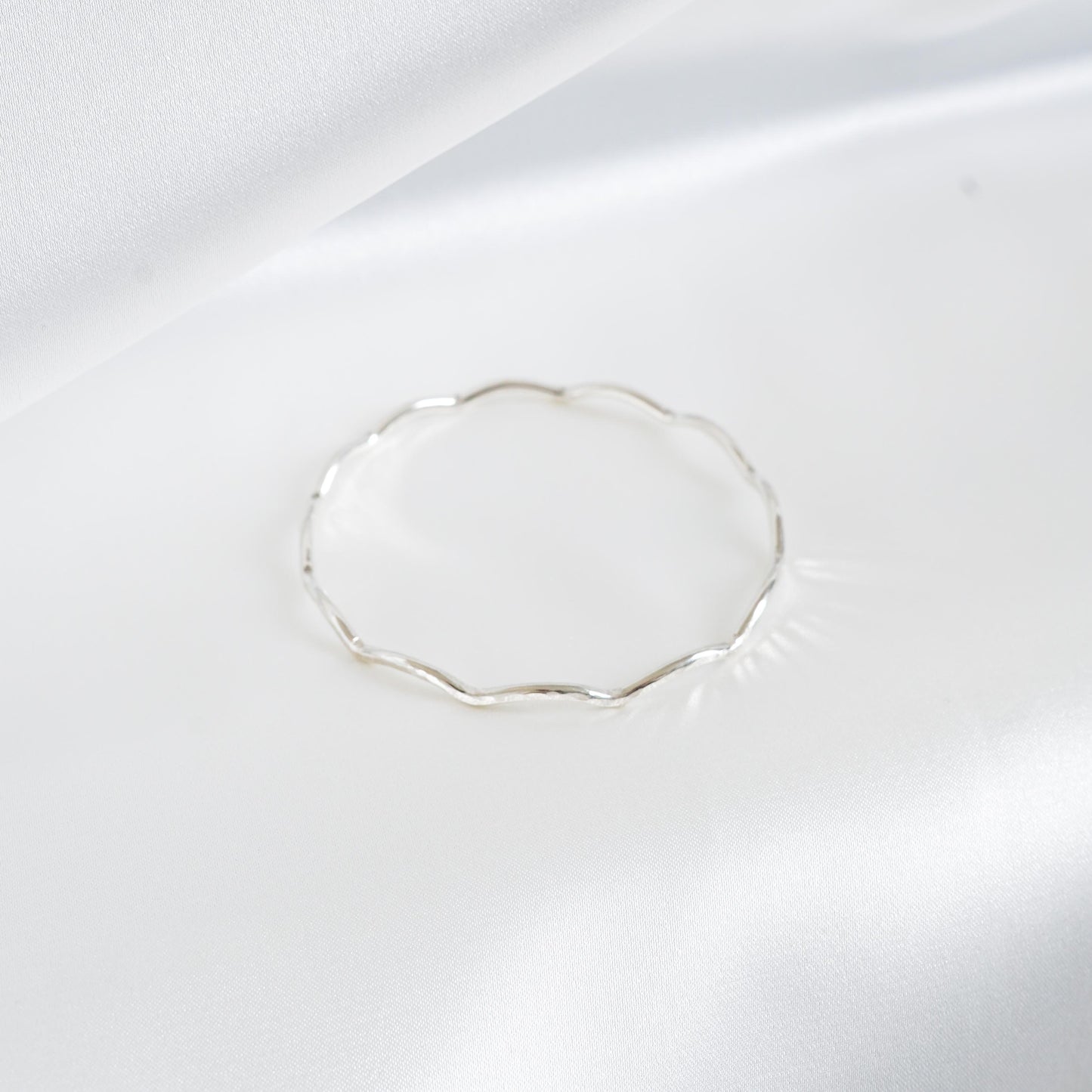 Silver wavy bracelet on a white satin background