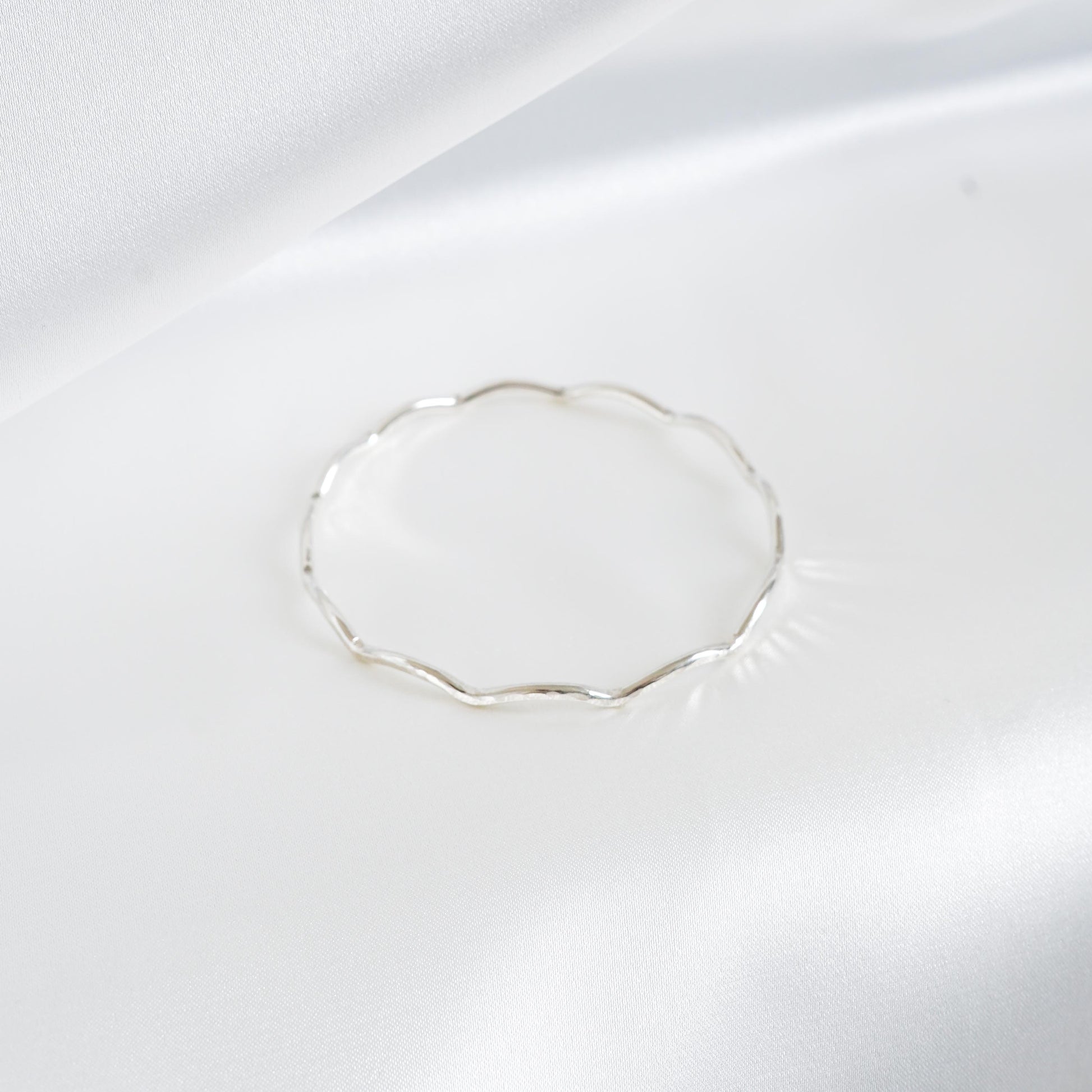 Silver wavy bracelet on a white satin surface