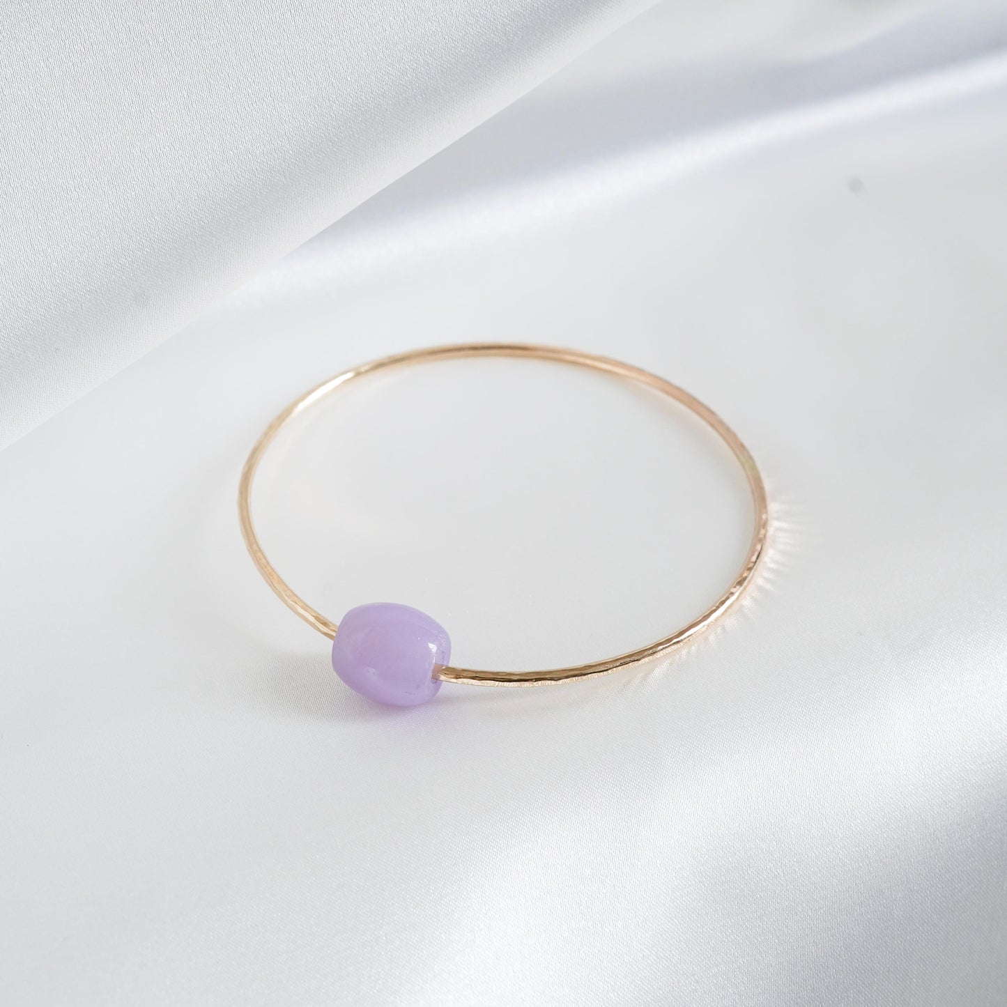 Gold bracelet with a purple jade bead on a white background