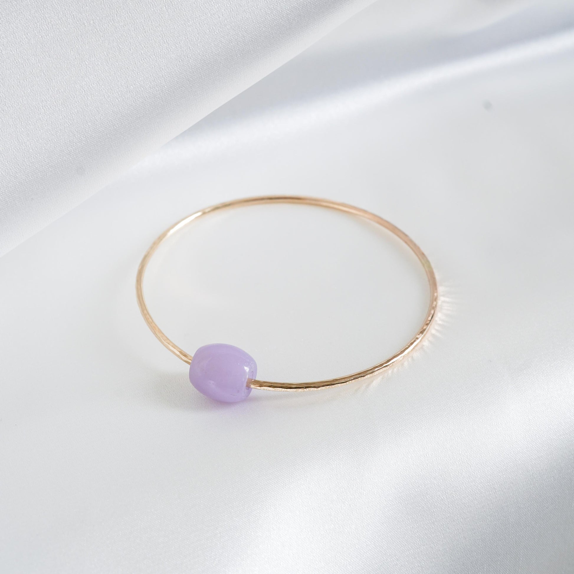 Gold bracelet with a purple jade bead on a white background