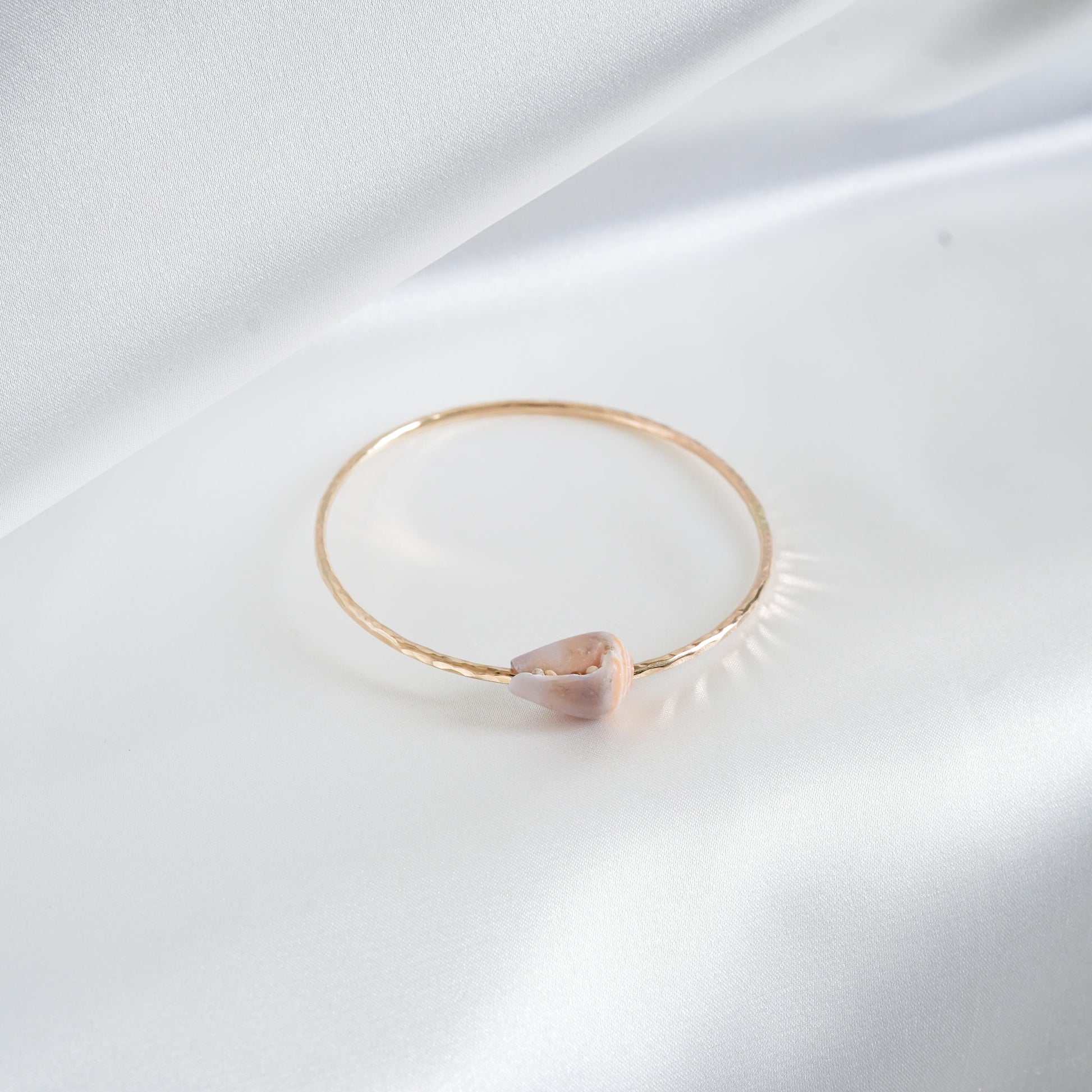 Gold bracelet with a pink white shell on a white background
