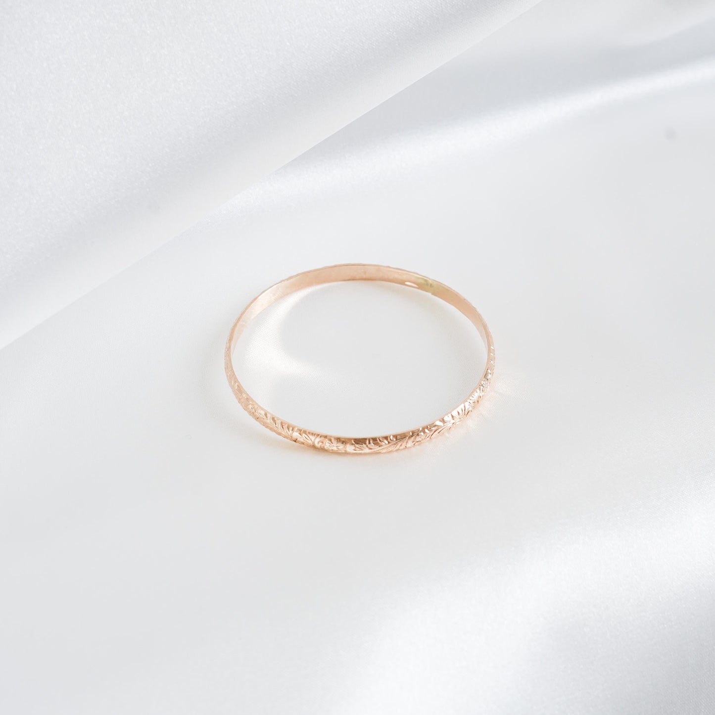 Gold bangle bracelet on white satin background