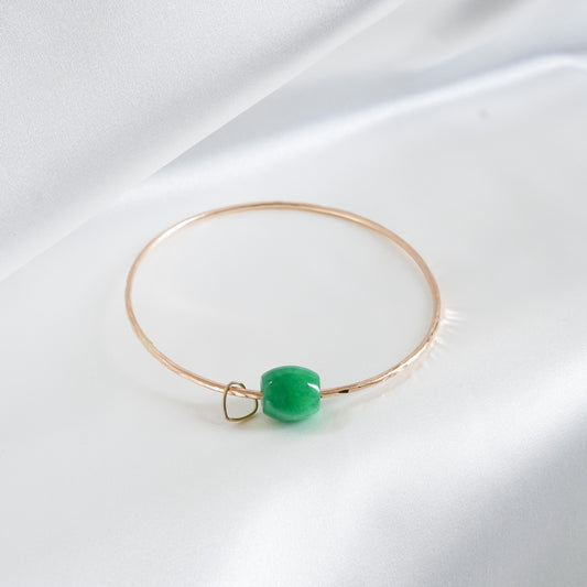 Gold bracelet with a green jade bead and heart charm on a white background