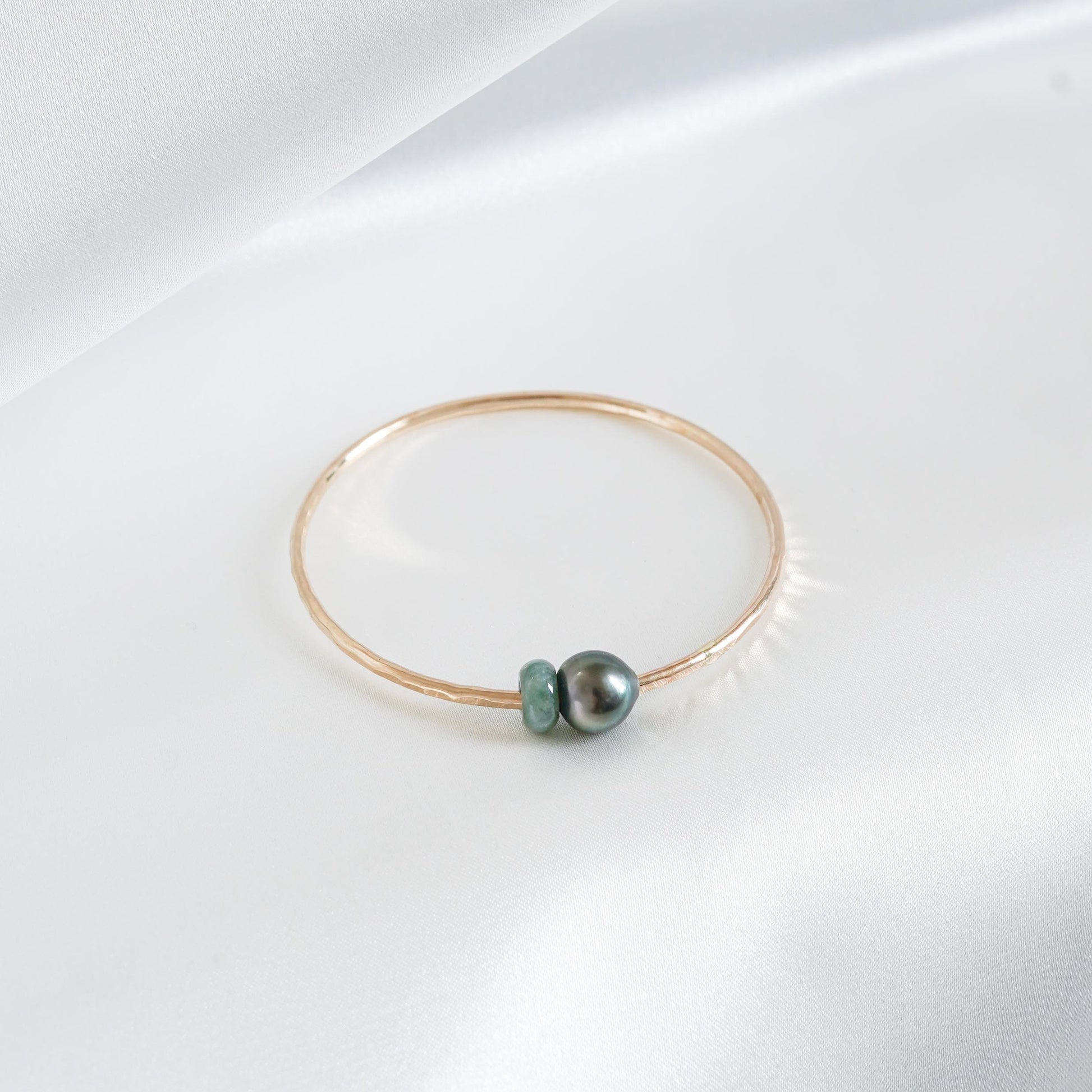 Gold bracelet with a single pearl and green jade charm on a white background