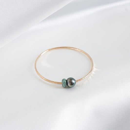 Gold bracelet with a single pearl and green jade charm on a white background