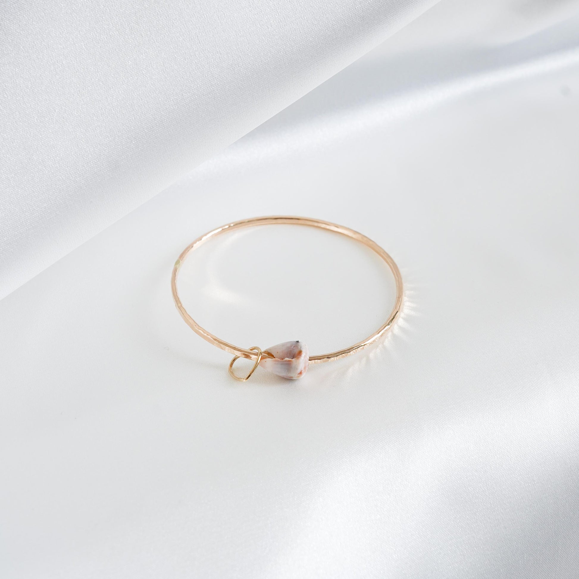 Gold bracelet with a heart-shaped charm and shell on a white background