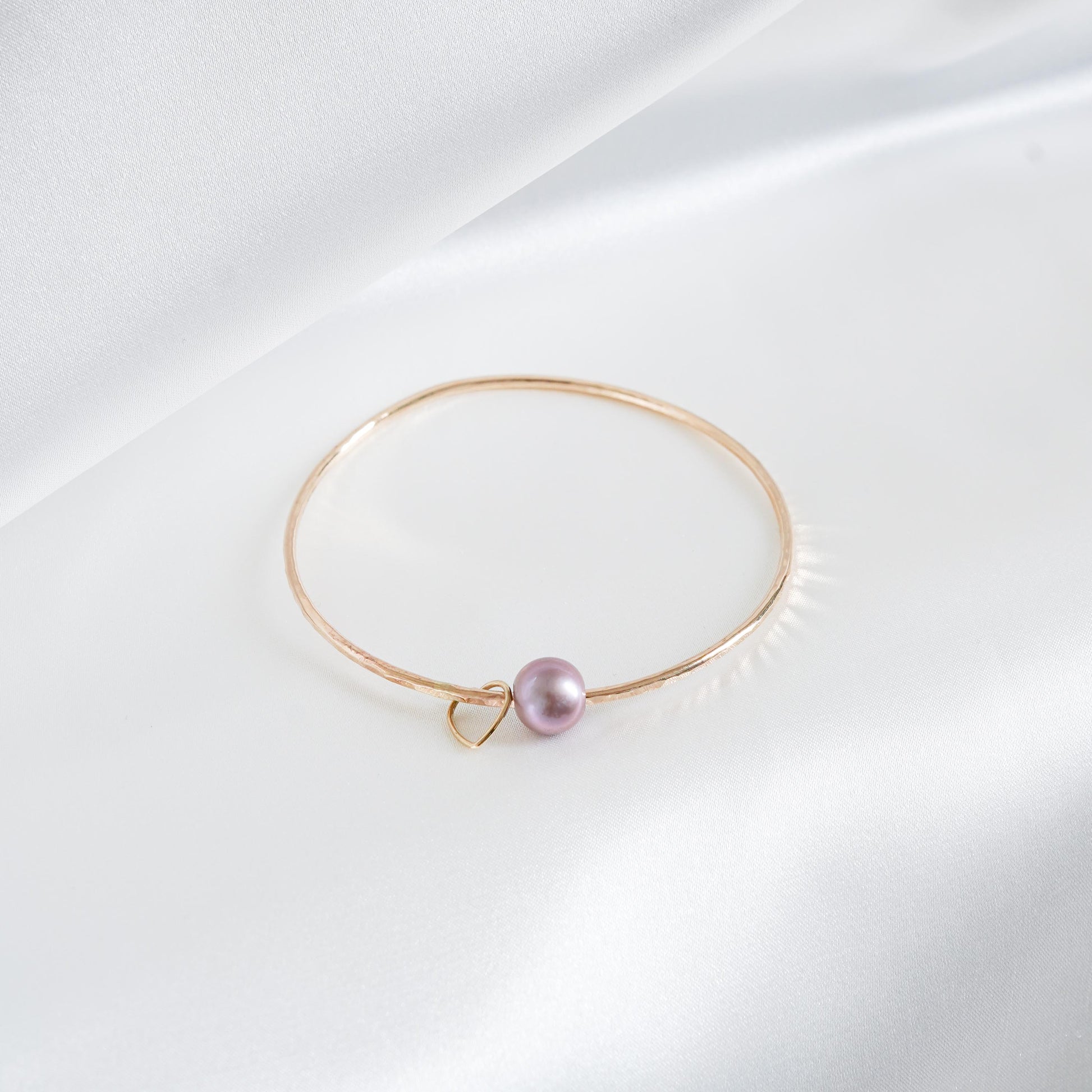 Gold bracelet with a single pearl and heart charm on a white background