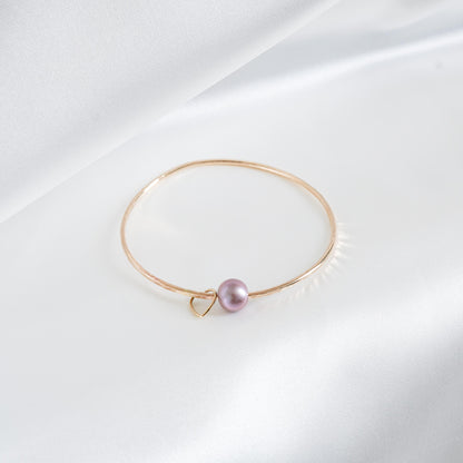 Gold bracelet with a single pearl and heart charm on a white background