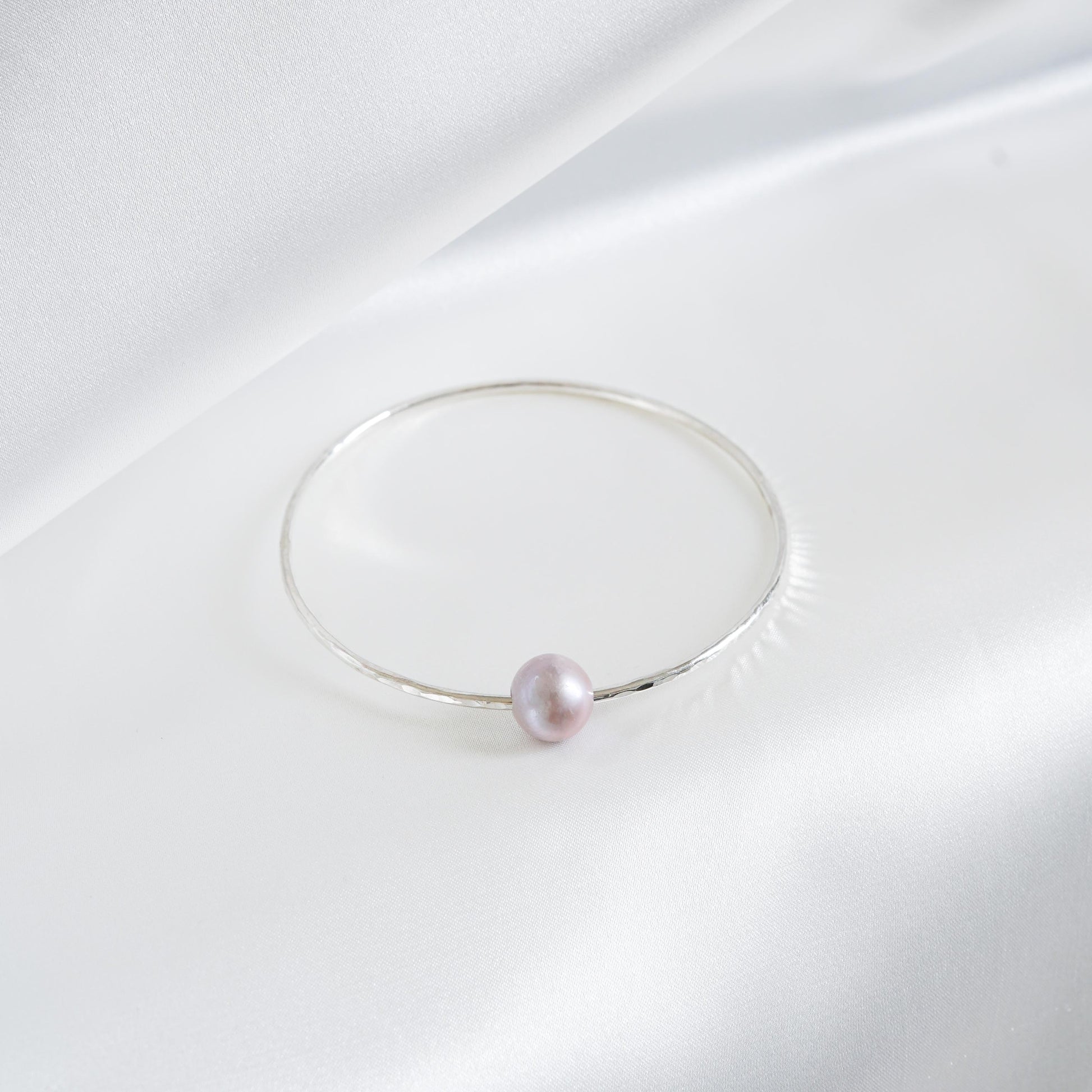 Silver bracelet with a single pearl on a white background
