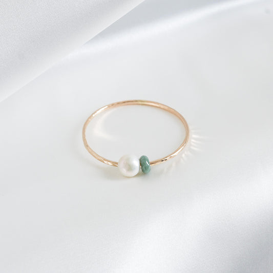 Gold bracelet with a single pearl and green jade charm on a white background