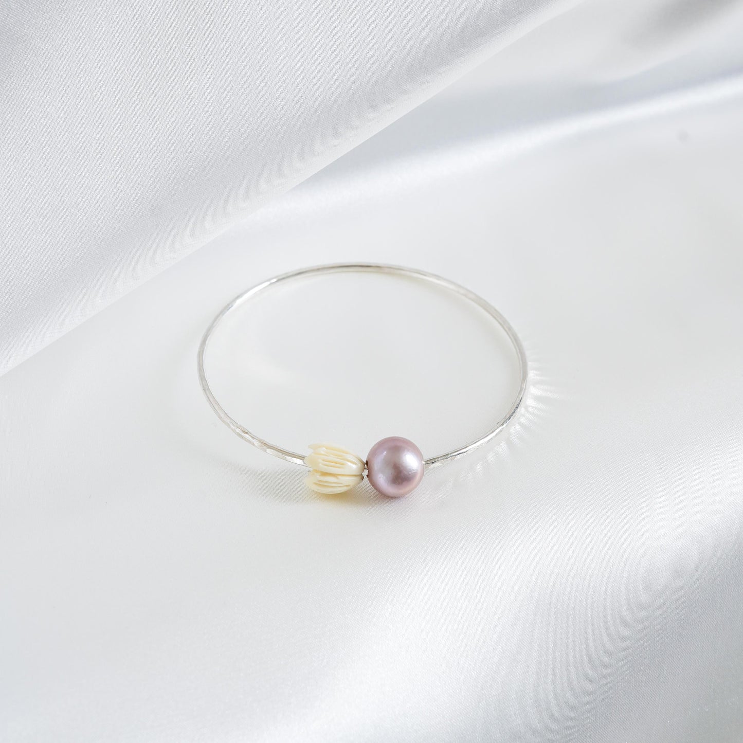 Silver bracelet with a pink pearl and white resin pikake flower bead on a white fabric background
