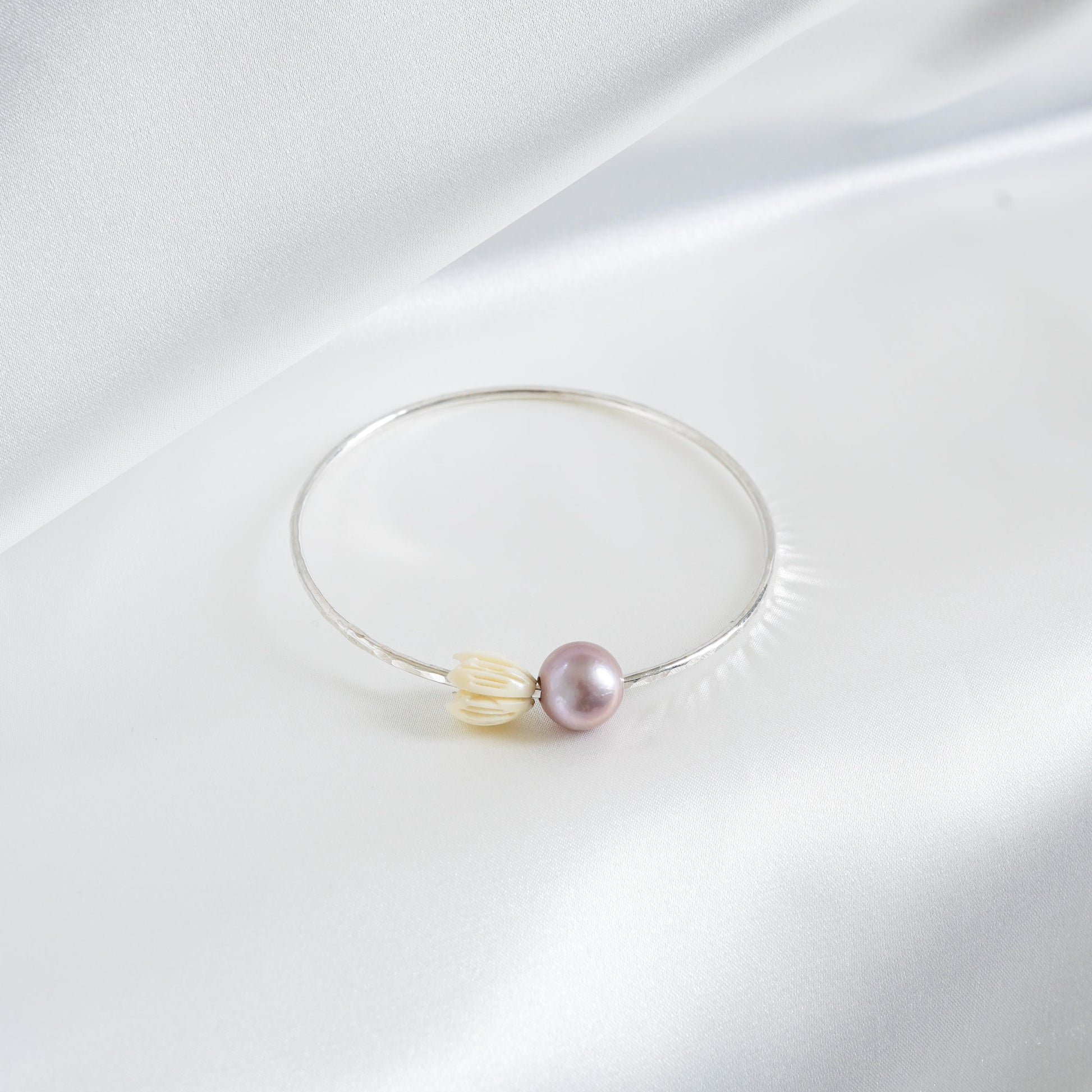 Silver bracelet with a pink pearl and white resin pikake flower bead on a white fabric background