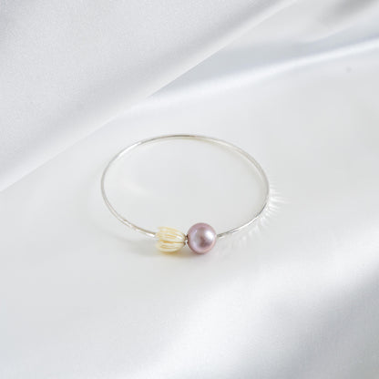 Silver bracelet with a pink pearl and white resin pikake flower bead on a white fabric background