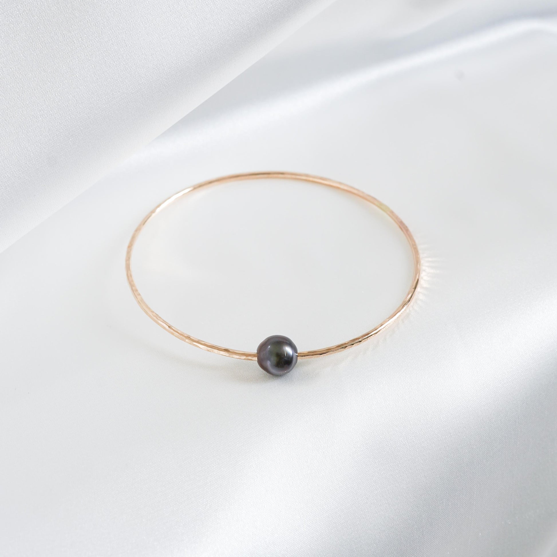 Gold bracelet with a single pearl on a white background