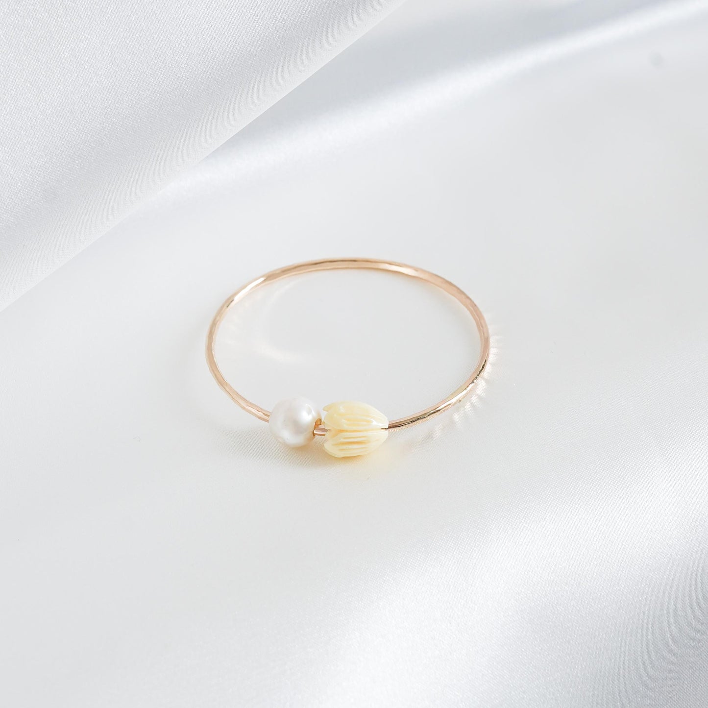 Gold bracelet with a pearl and tan pikake flower bead on a white background