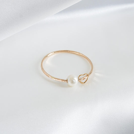 Gold bracelet with a white pearl and heart charm on a white background
