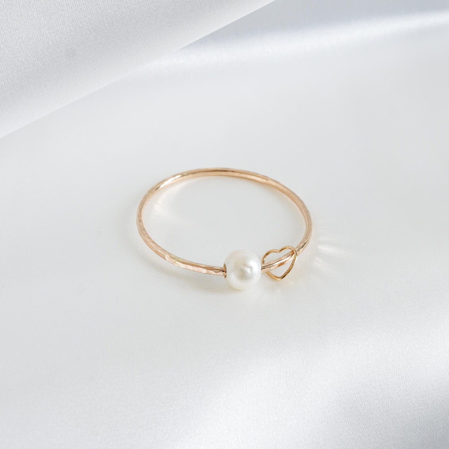Gold bracelet with a pearl and heart charm on a white background