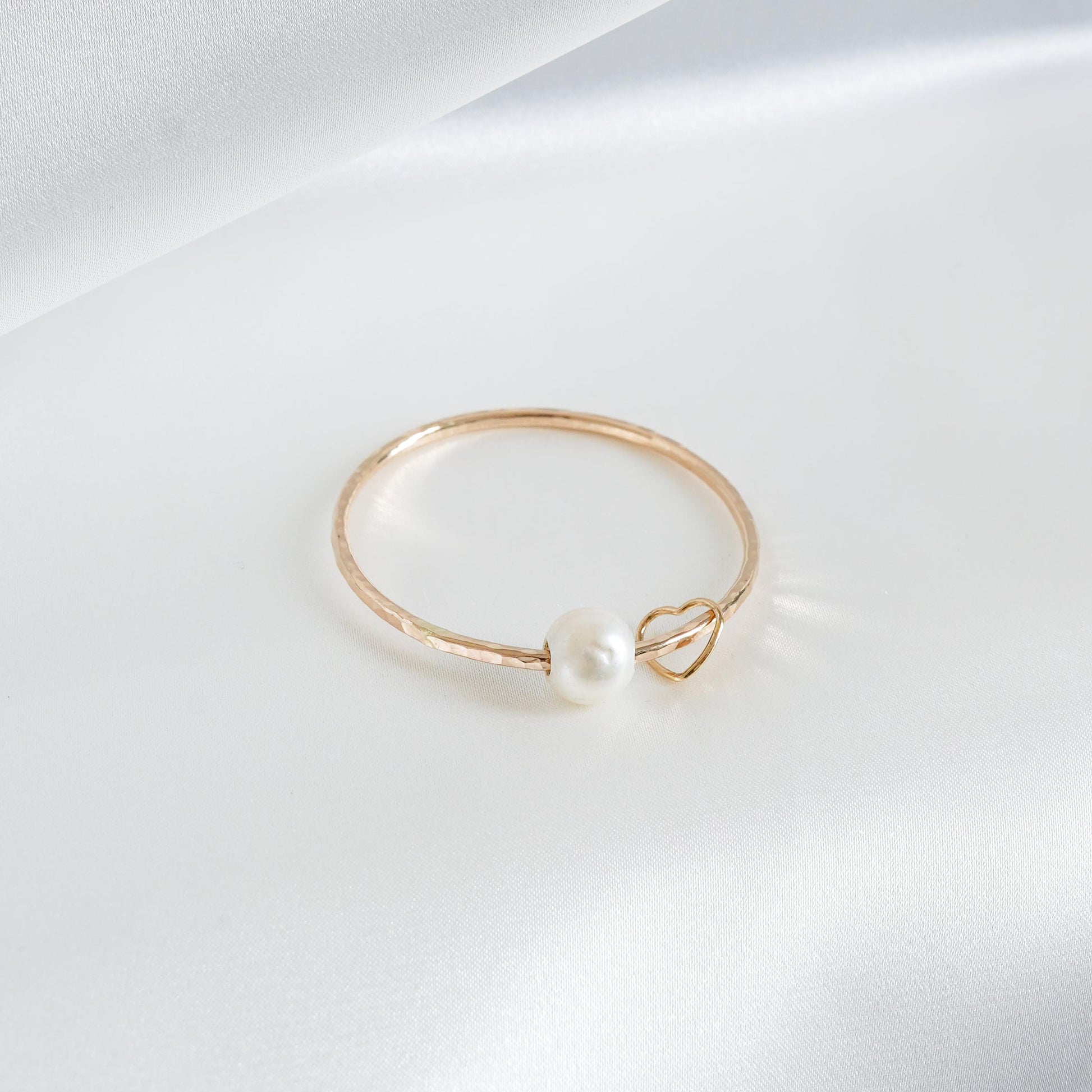 Gold bracelet with a pearl and heart charm on a white background