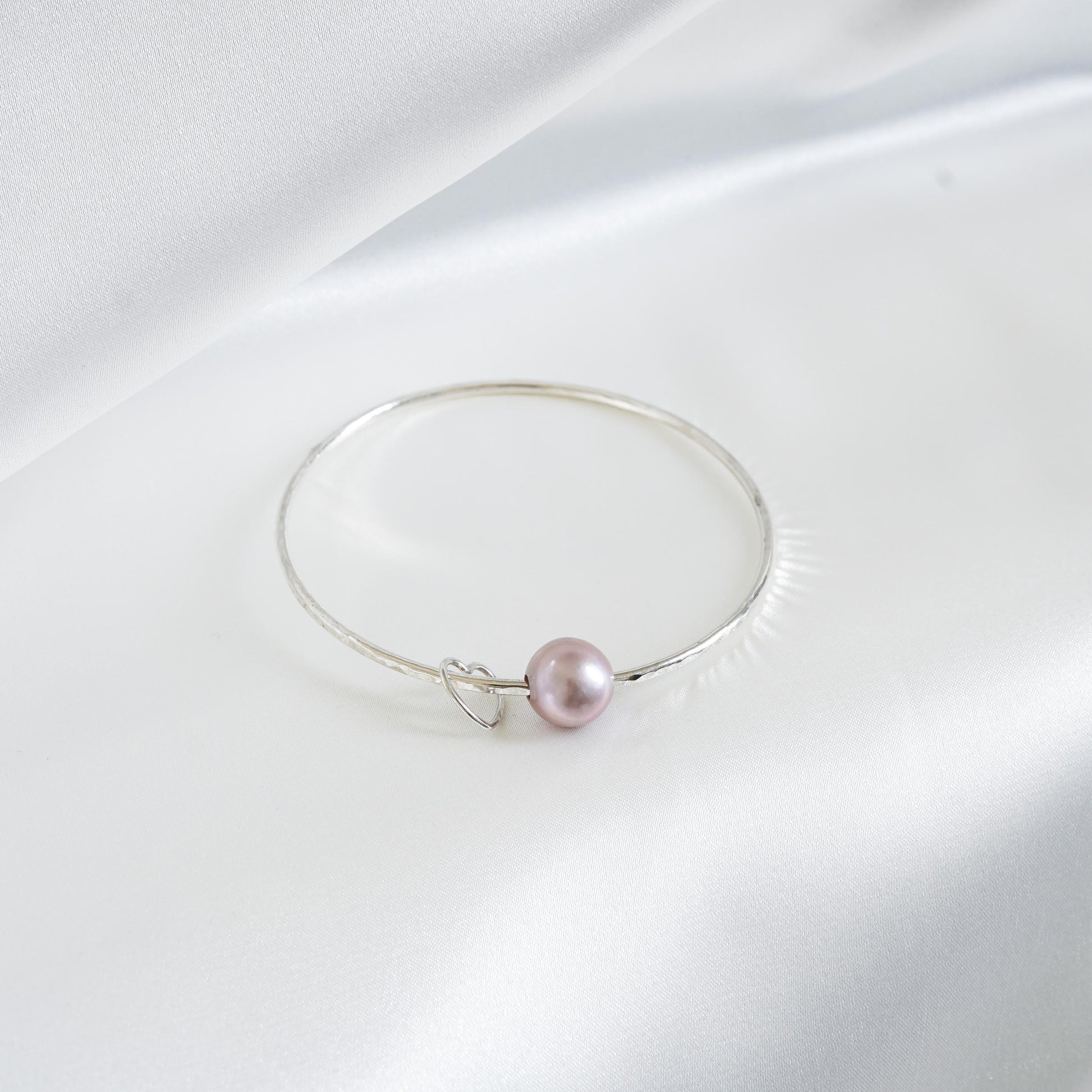 Silver bracelet with a single pearl and heart charm on a white background