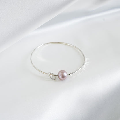 Silver bracelet with a single pearl and heart charm on a white background