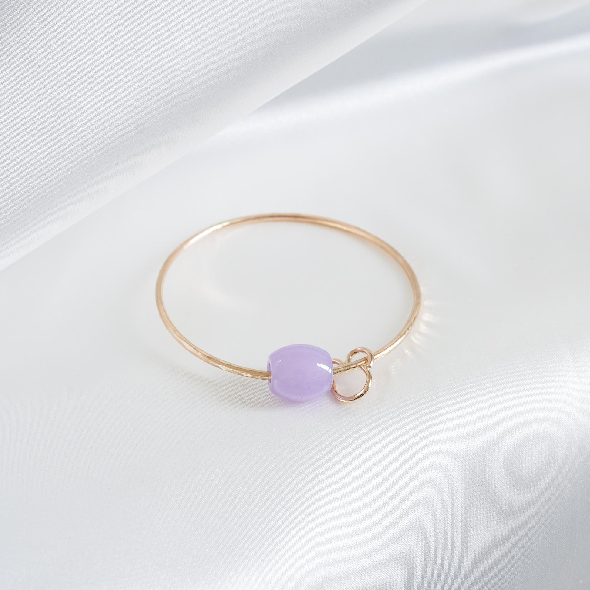 Gold bracelet with a purple jade bead and mickey mouse charm on a white background