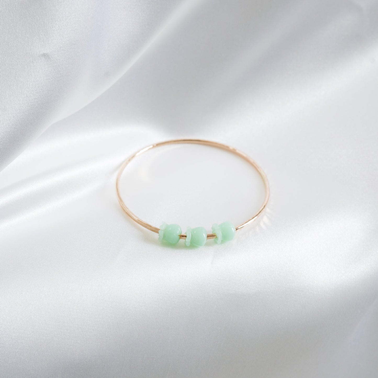 Gold bracelet with green crown flower beads on a white fabric background