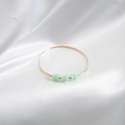 Gold bracelet with green crown flower beads on a white fabric background