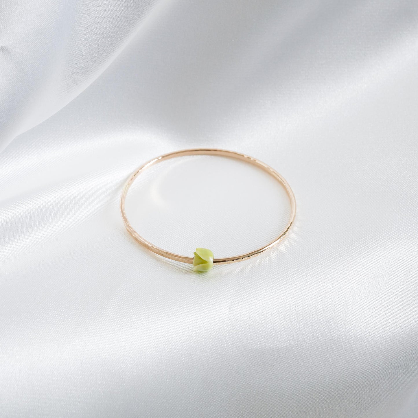 Gold bracelet with a green flower bead on a white fabric background