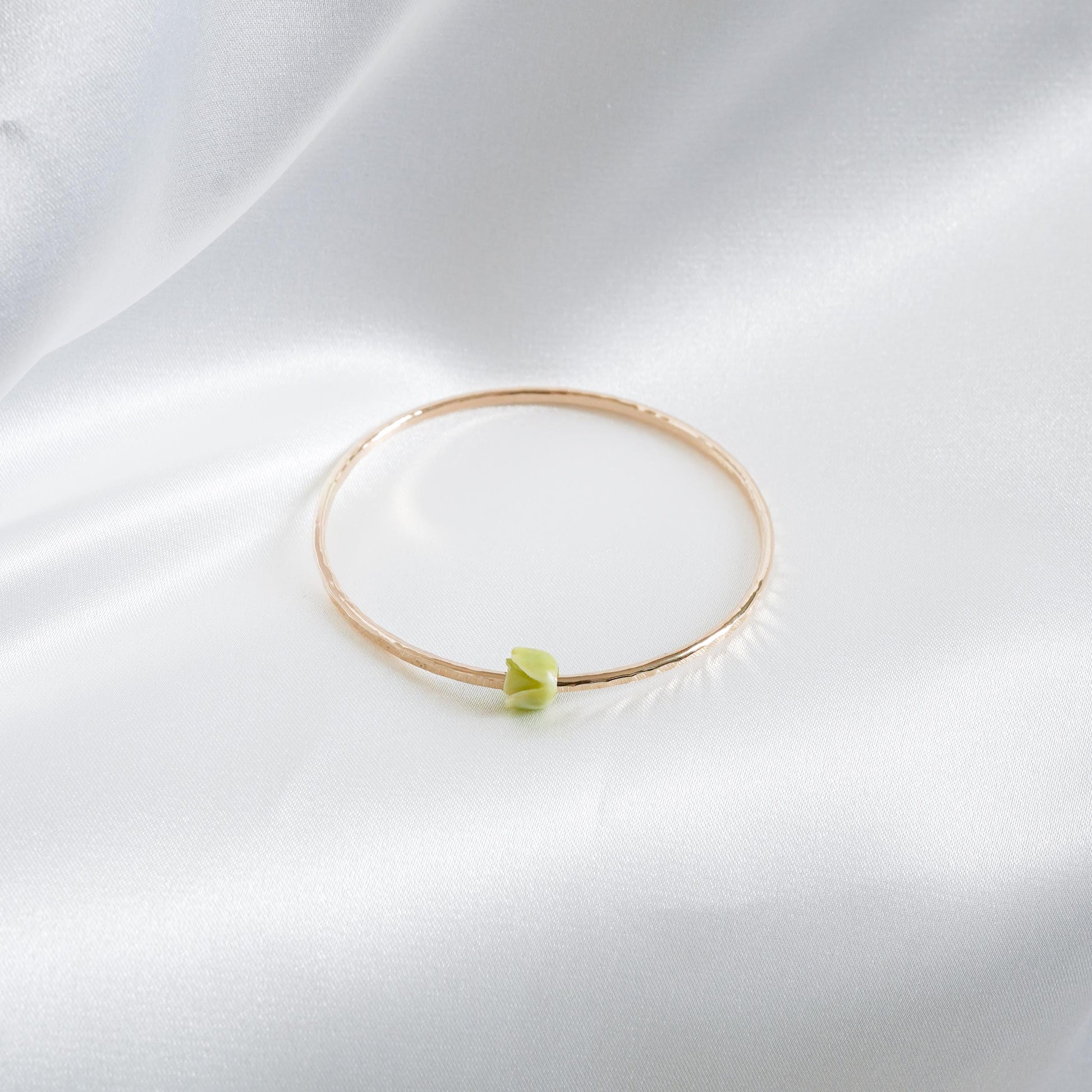 Gold bracelet with a green flower bead on a white fabric background