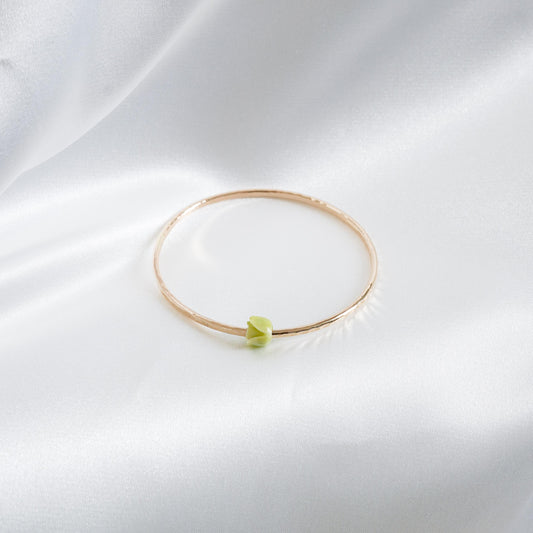 Gold bracelet with a green flower bead on a white fabric background