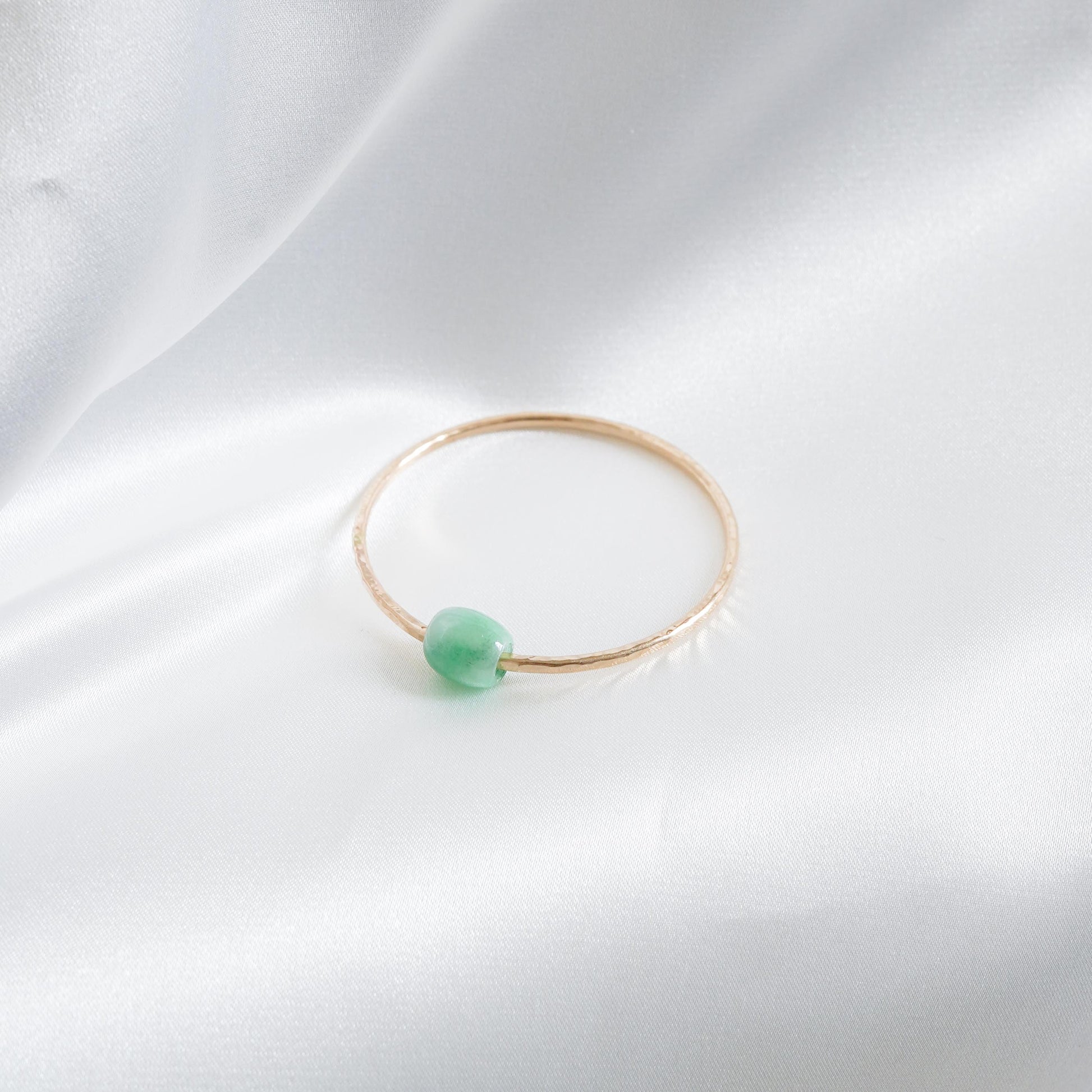 Gold bracelet with a green jade bead on a white fabric background