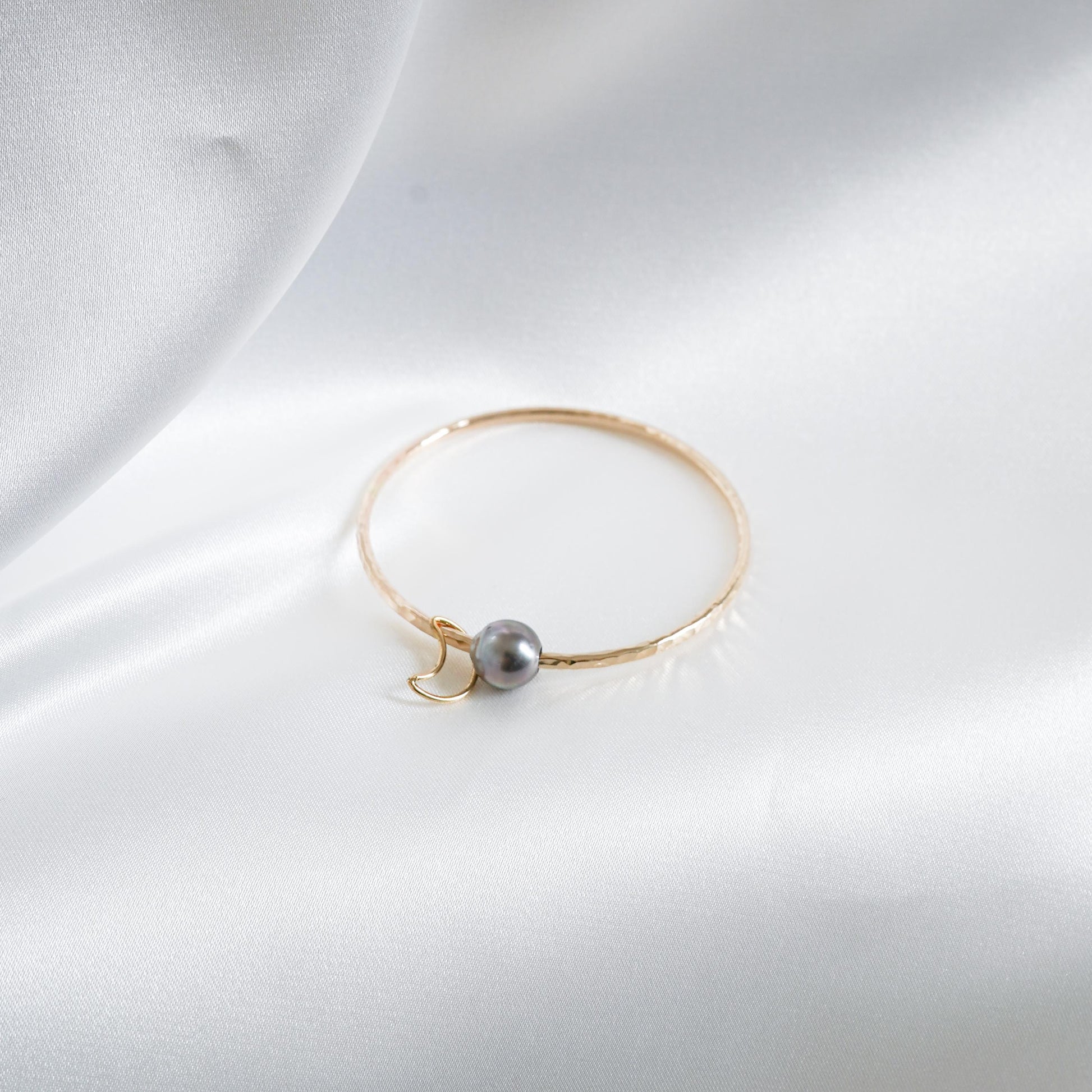 Gold bracelet with a single pearl and moon charm on a white background