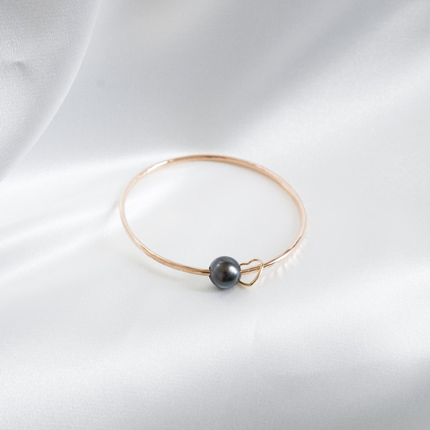 Gold bracelet with a single pearl and heart charm on a white background