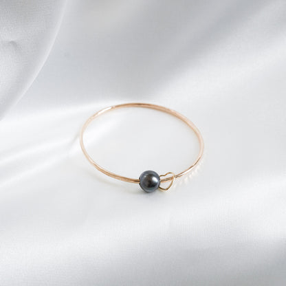Gold bracelet with a single pearl and heart charm on a white background