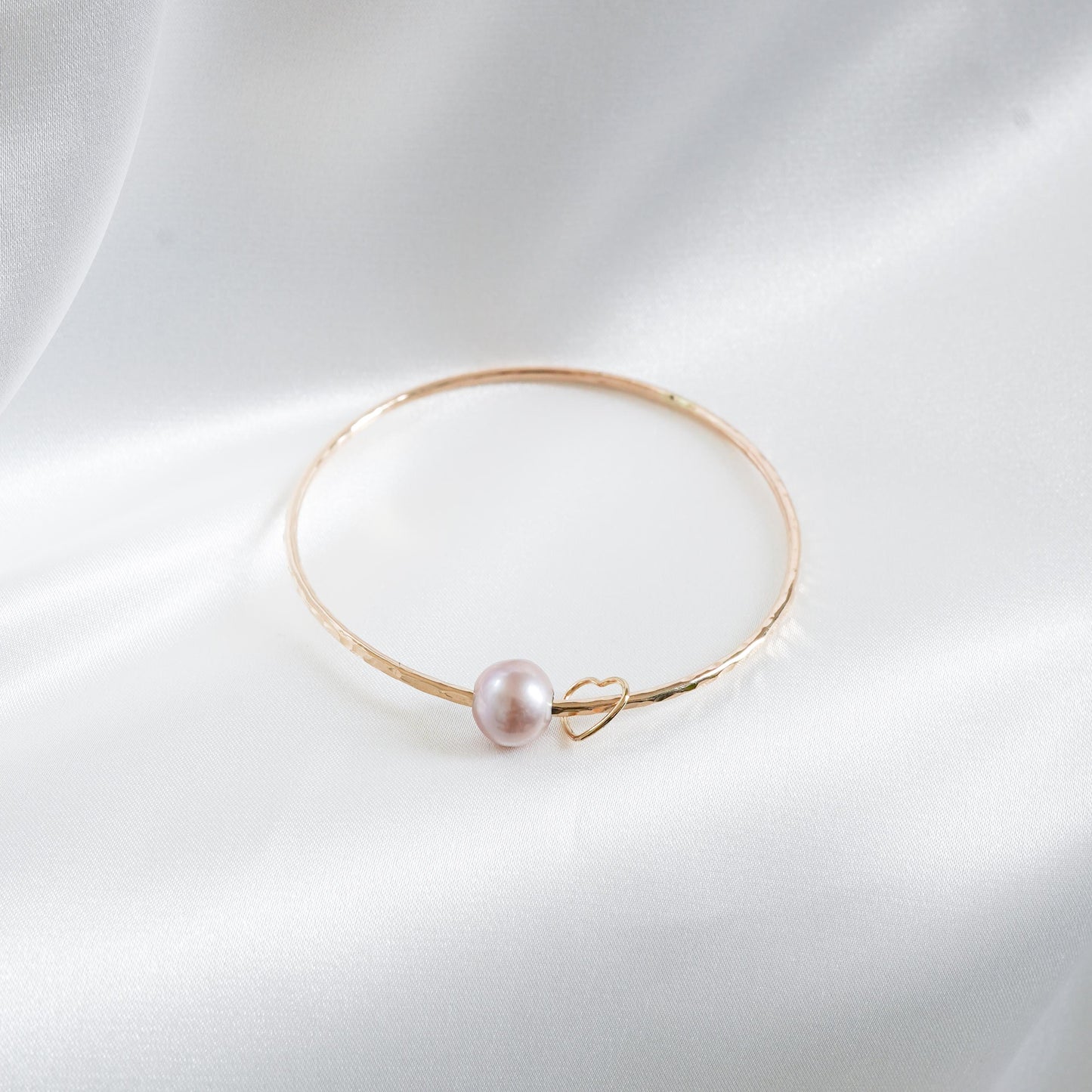Gold bracelet with a single pearl and heart charm on a white background