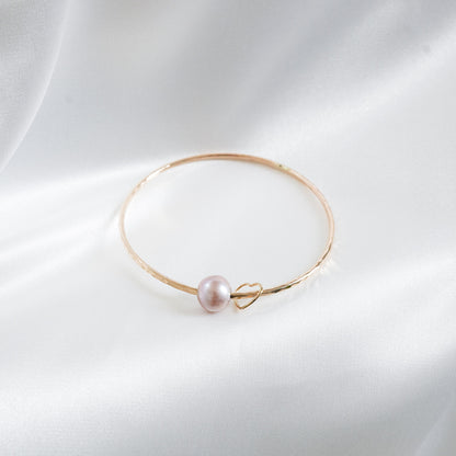Gold bracelet with a single pearl and heart charm on a white background