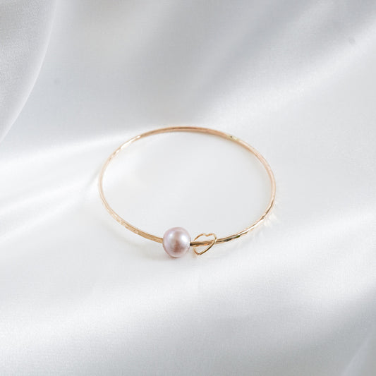 Gold bracelet with a single pearl and heart charm on a white background