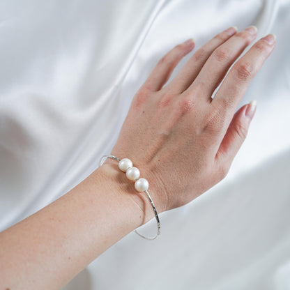 Hand wearing a triple pearl bracelet on a white fabric background
