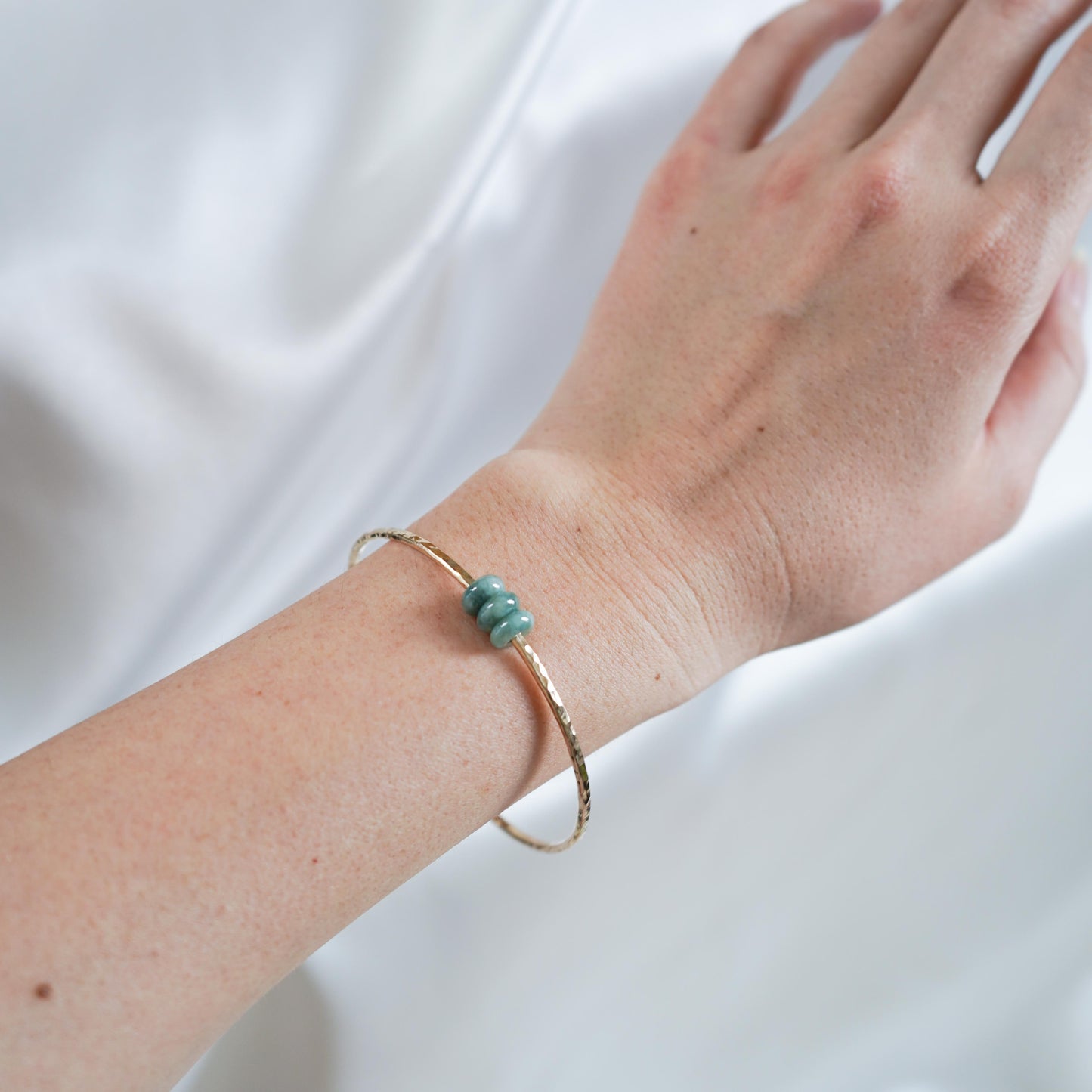Hand wearing a gold bangle with three jade donut beads
