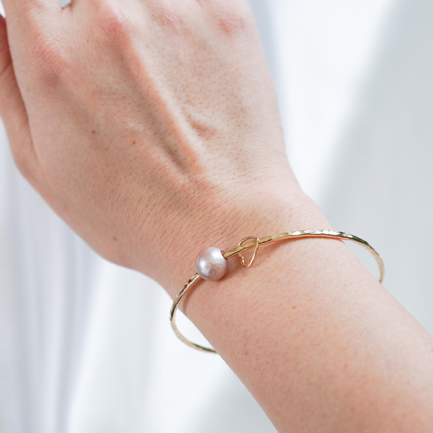 Gold bracelet with a pink pearl on a wrist against a white background