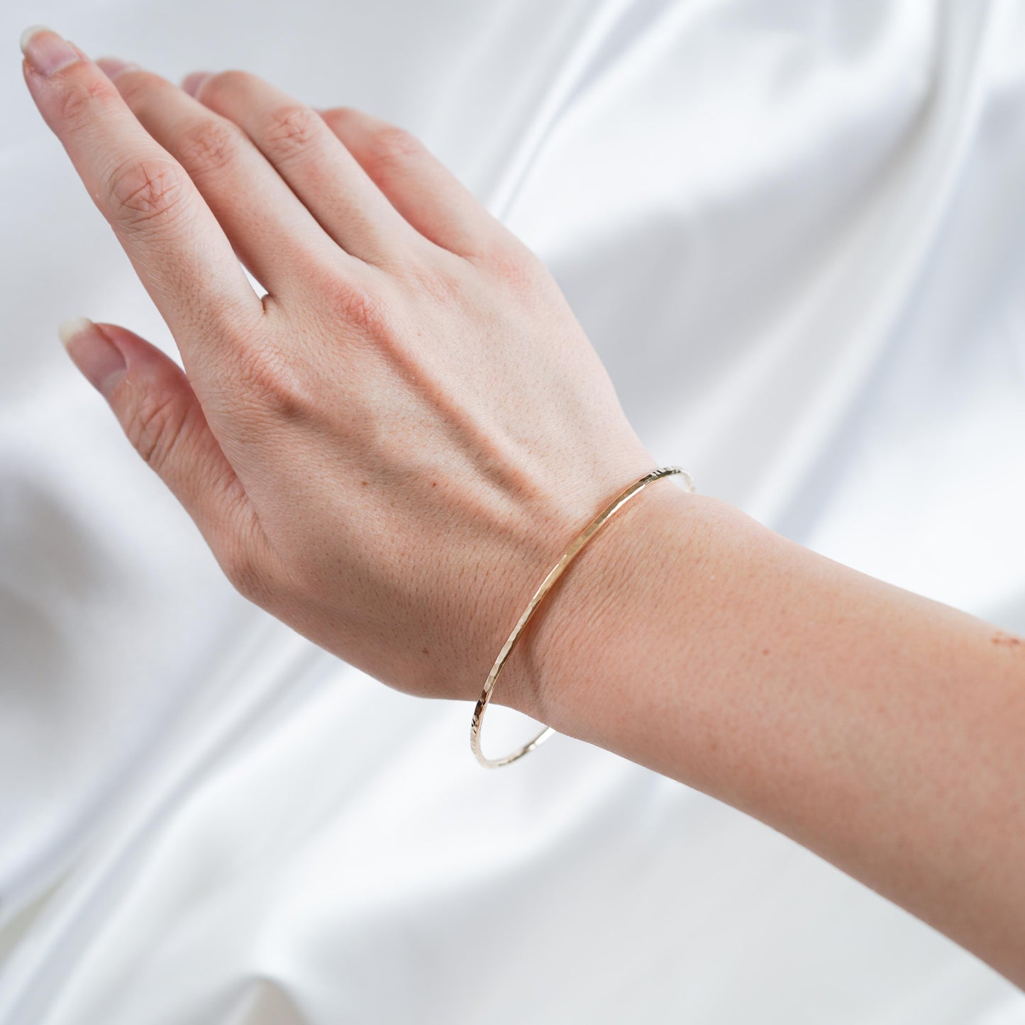 Gold bracelet on a person's wrist against a white background
