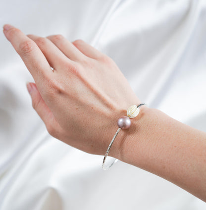 Silver bangle with pink pearl and tan pikake bead on a wrist against white satin background