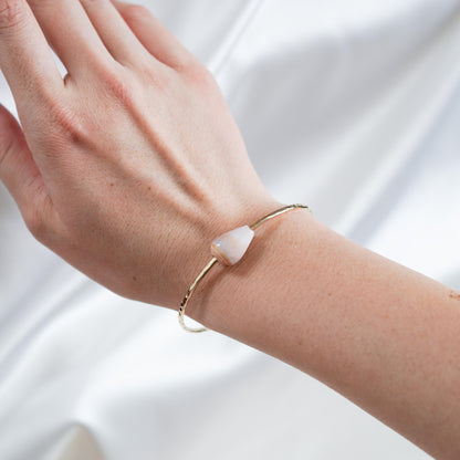 Gold bracelet with a white shell on a person's wrist against a white background