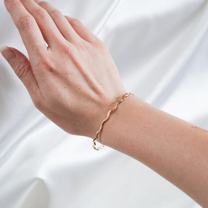 gold wavy bangle on wrist against white satin fabric