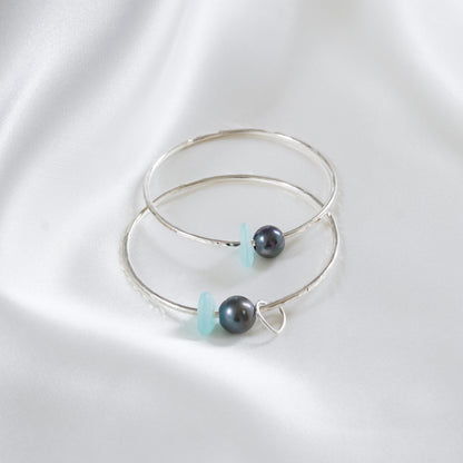 Two silver bangles with tahitian pearls and blue sea glass on a white background